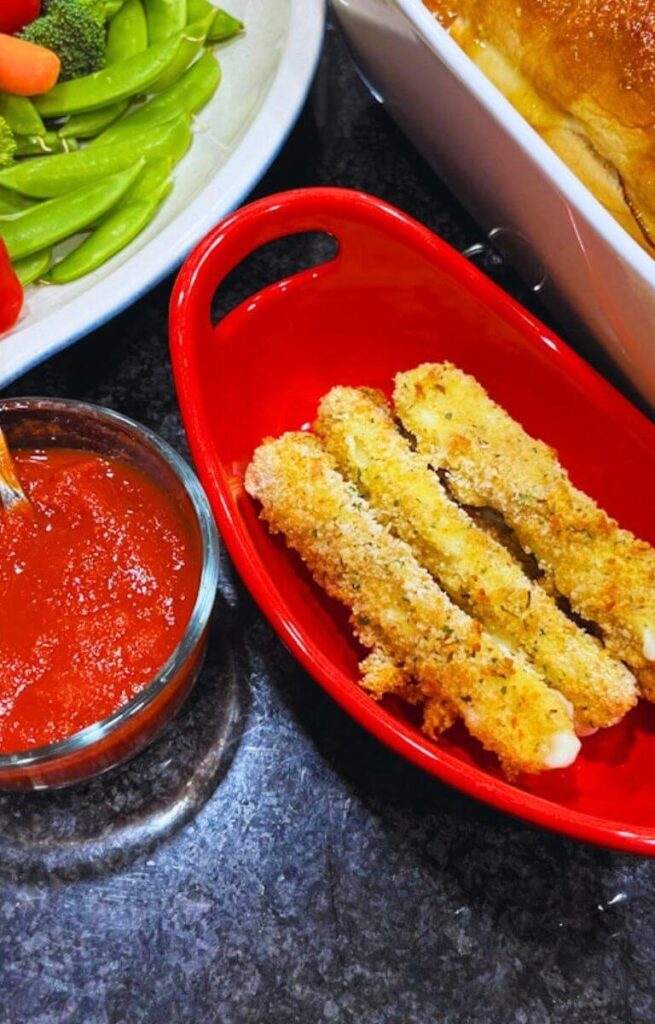close up of mozzarella sticks next to a small bowl of marinara sauce.