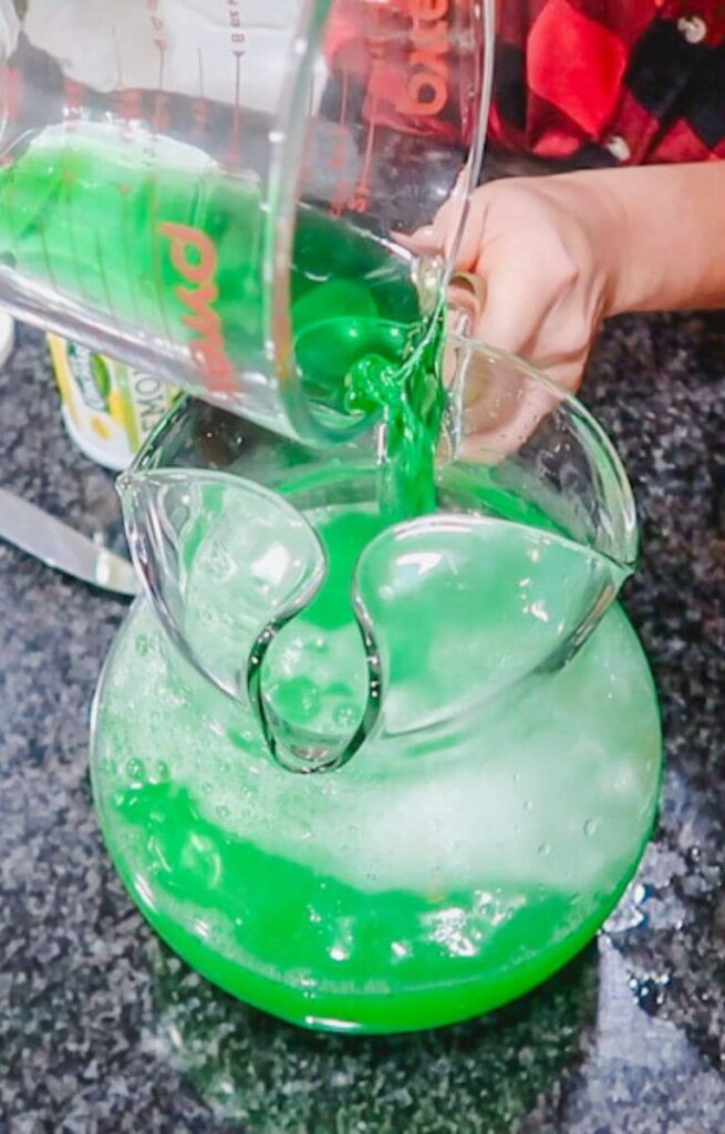 a measuring cup pouring lime green jello into a glass pitcher