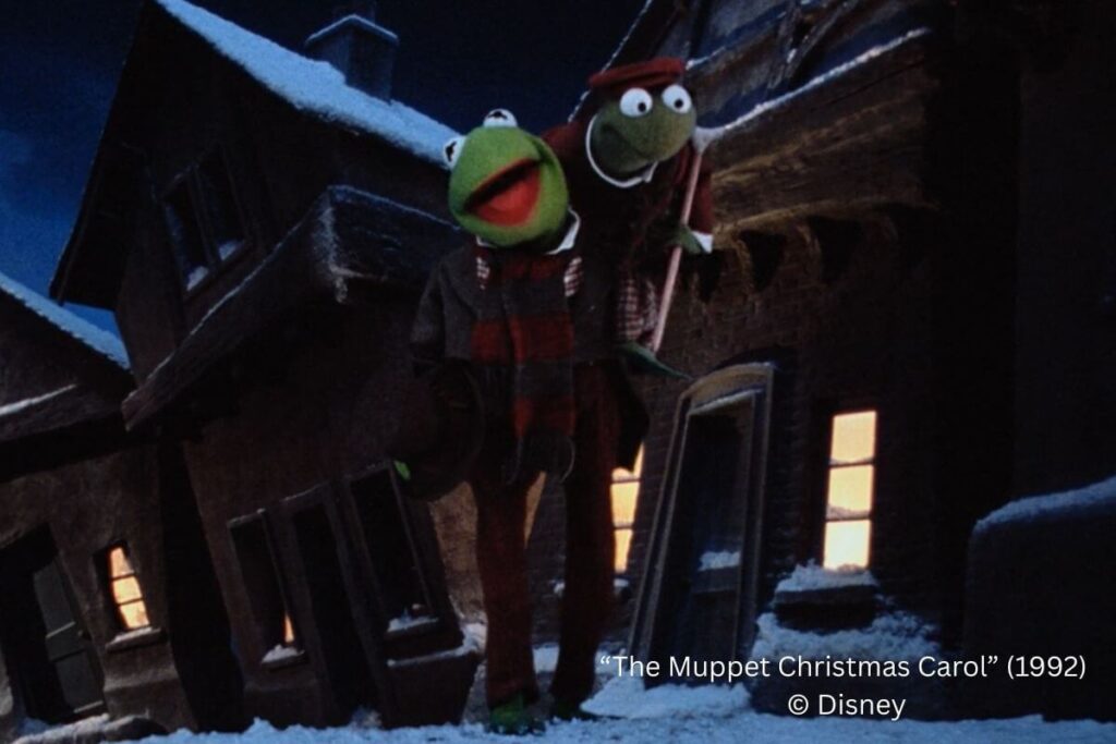Bob Cratchit (Kermit) and Tiny Tim (Robin) walking in the snow-lined street.