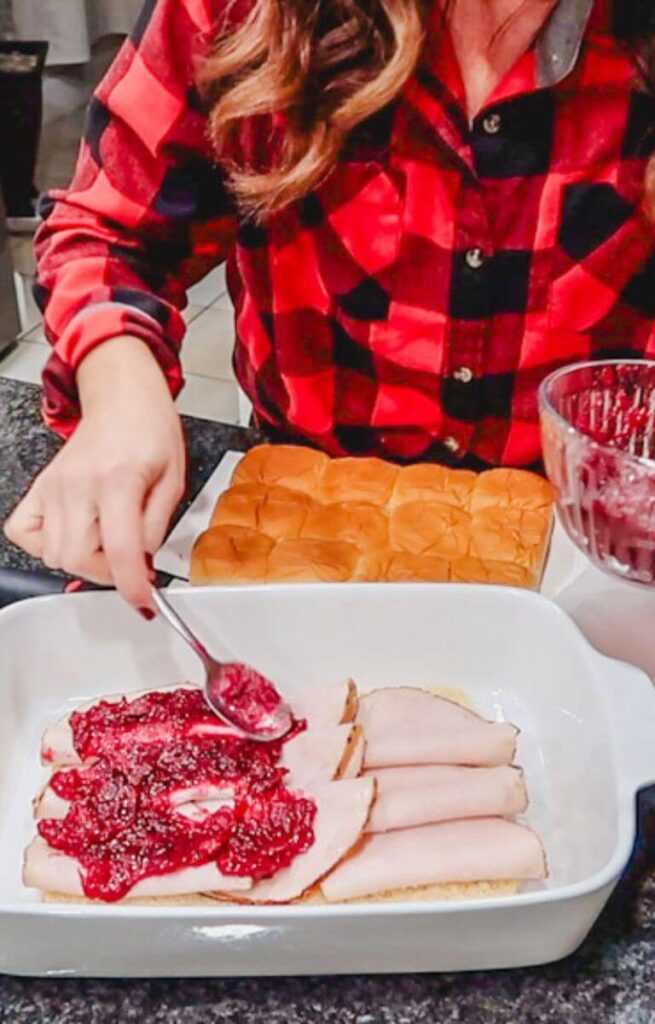 spreading homemade cranberry sauce over sliced turkey in a baking dish.