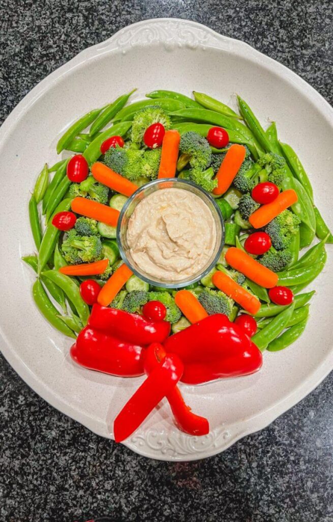 overhead shot of a wreath made of vegetables with hummus in the middle of the platter.