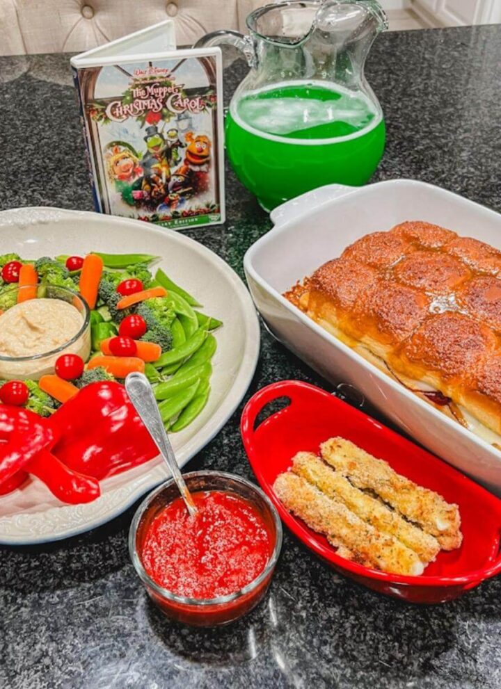 overhead image of a vegetable platter, sliders, mozzarella sticks, and green punch on a black counter for The Muppet Christmas Carol movie night.