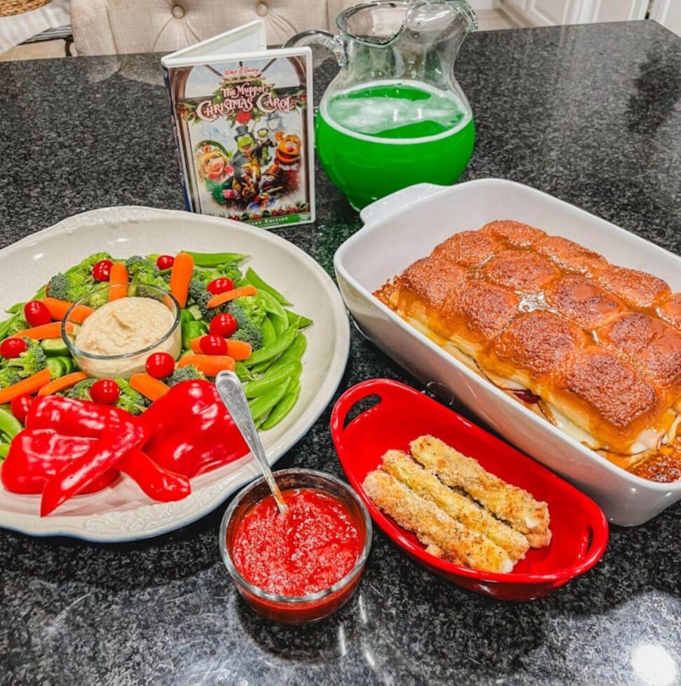 overhead image of a vegetable platter, sliders, mozzarella sticks, and green punch on a black counter for The Muppet Christmas Carol movie night.