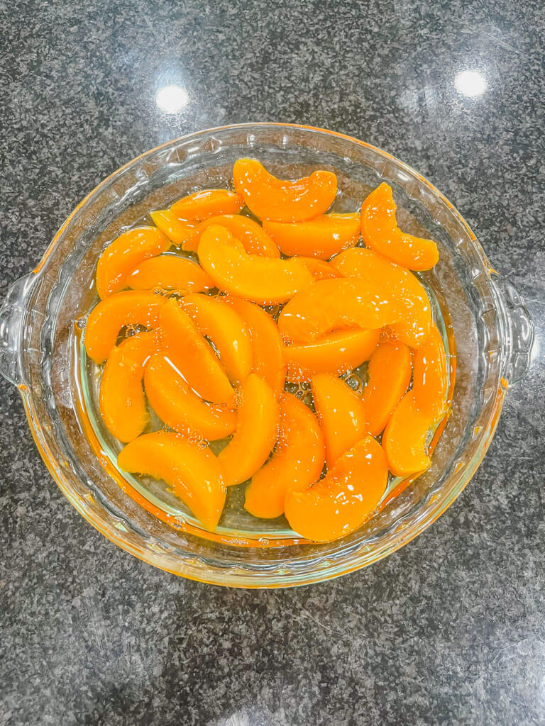 canned peaches with juices in a glass pie dish.