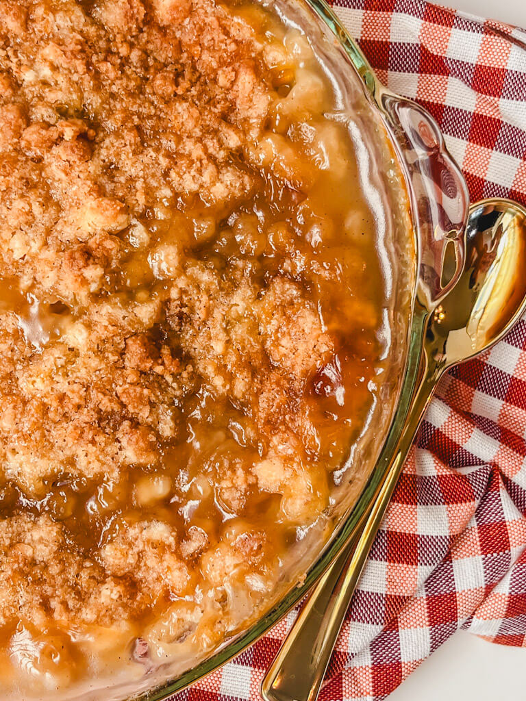 overhead view of peach crumble on a striped towel with a gold spoon next to the pie dish.