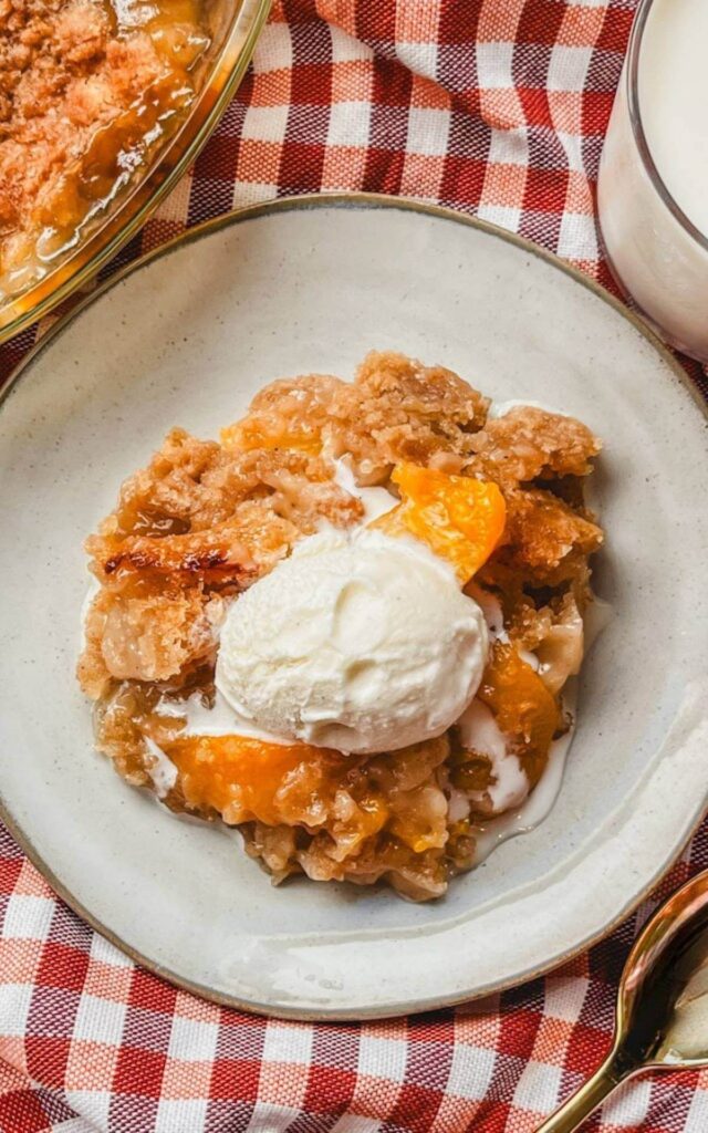 overhead view of a serving of peach crumble on a white plate next to a glass of milk.