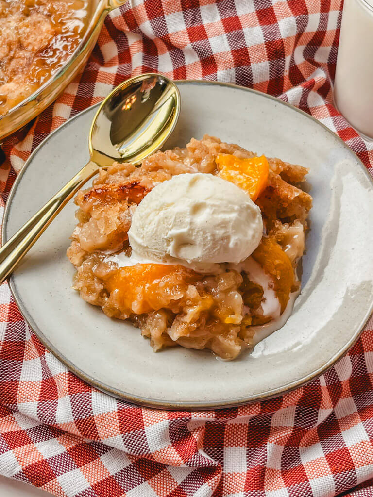 a serving of peach crumble on a white plate next to a gold spoon.