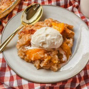 a serving of peach crumble without oats on a white plate with a gold spoon next to it.