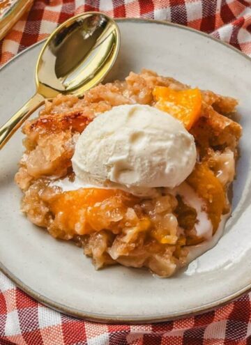 a serving of peach crumble without oats on a white plate with a gold spoon next to it.
