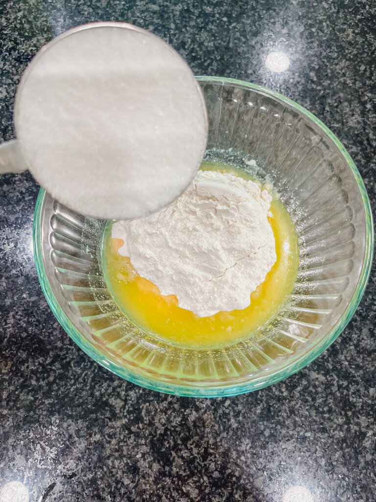 a measuring cup filled with sugar about to be added to the glass bowl.