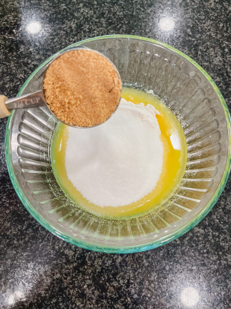 a measuring cup holding brown sugar over the bowl of butter, flour and sugar