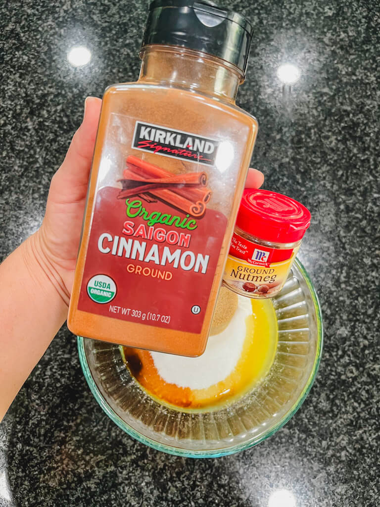 a bottle of cinnamon and nutmeg being held over the bowl of melted butter.
