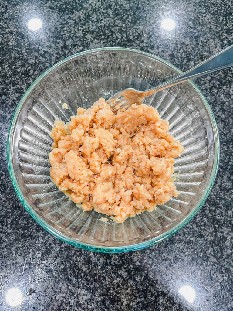 a fork in a bowl with the crumble mixture for peach crumble without oats.