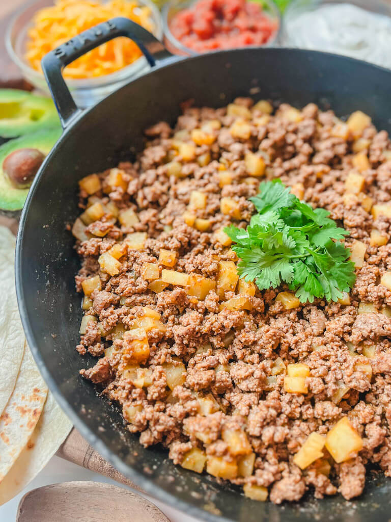 close up shot of beef and potato burrito filling in a cast iron skillet with cilantro on top.