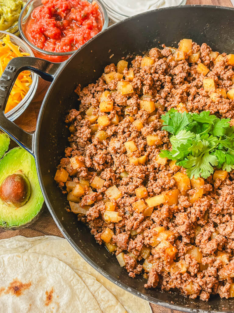 beef and potato burrito filling in a skillet with cilantro on top.