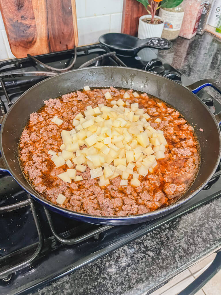 diced potatoes added to the skillet of ground beef mixture simmering.