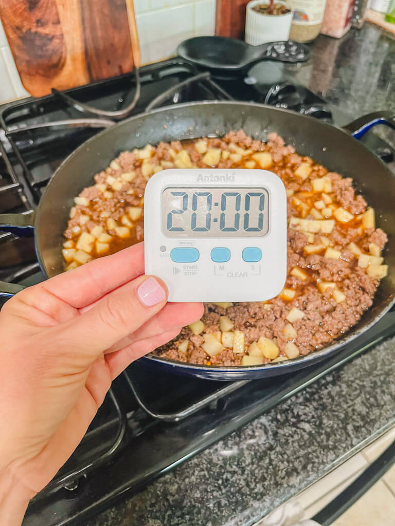 a timer with 20 minutes being held in front of the skillet.
