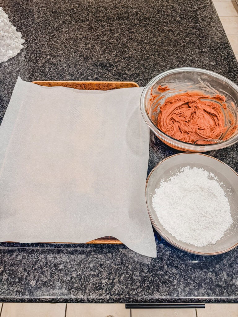 assembly line of batter, powdered sugar and prepared baking dish for the chocolate crinkle cookies.