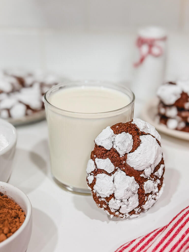 close up of a cookie standing up and laying against a glass of milk.