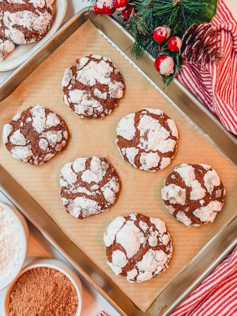 overhead shot of chocolate crinkle cookies on a baking sheet next to a red striped Christmas kitchen towel.