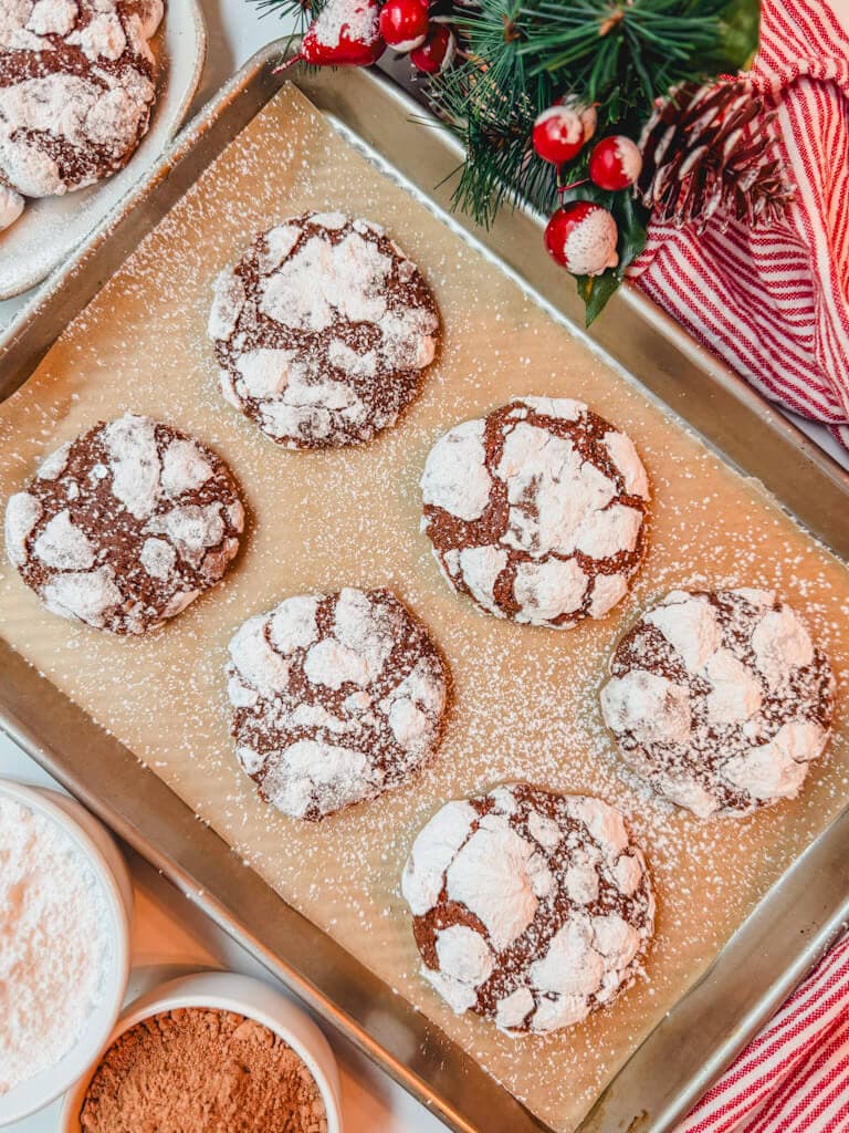 six crinkle cookies on a baking sheet that have been dusted with additional powdered sugar.
