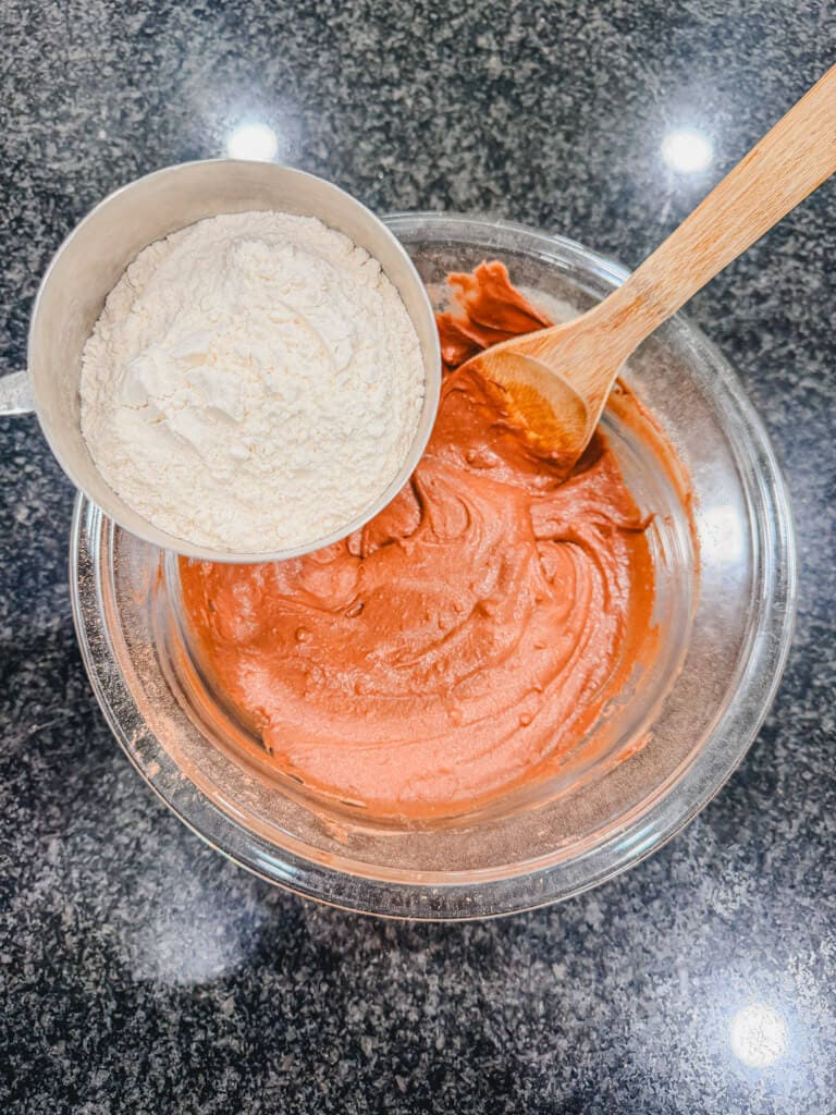 A measuring cup, holding flour over the mixing bowl.