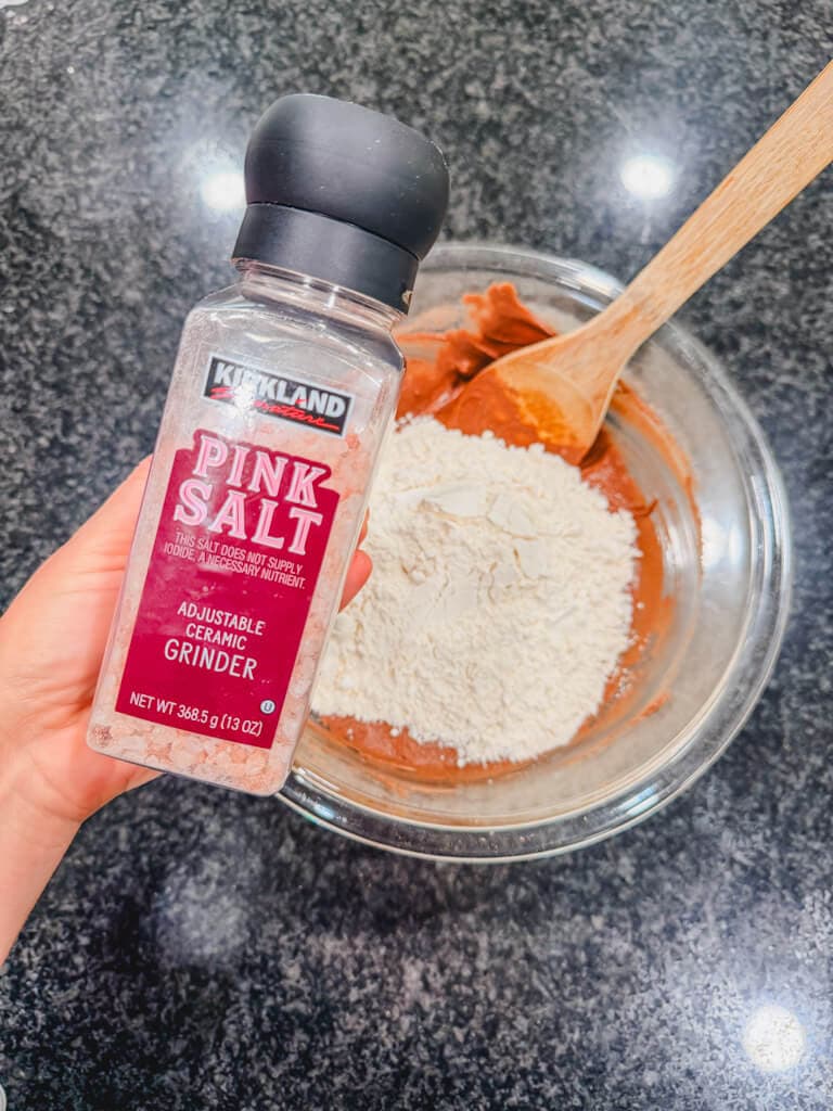 a bottle of salt being held over the mixing bowl.