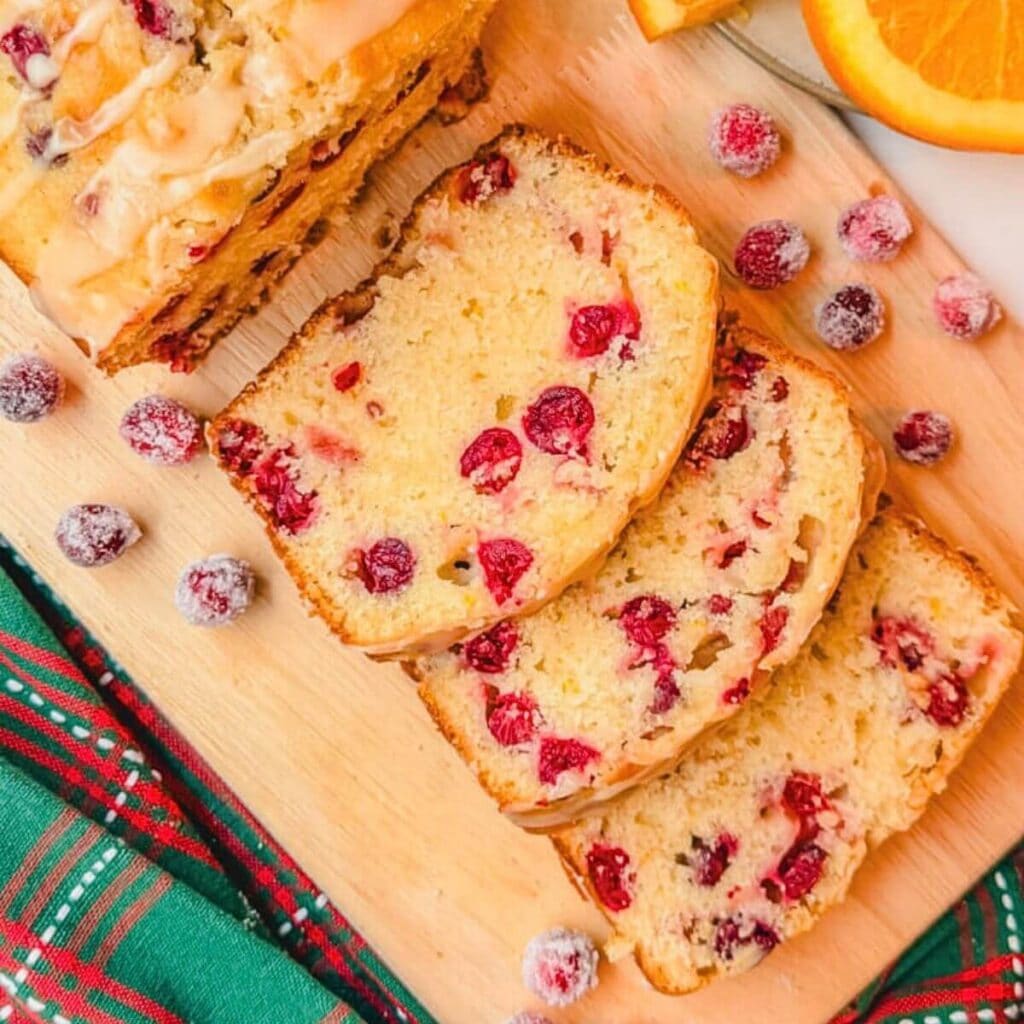 three slices of cranberry orange loaf on a cutting board next to candied cranberries.