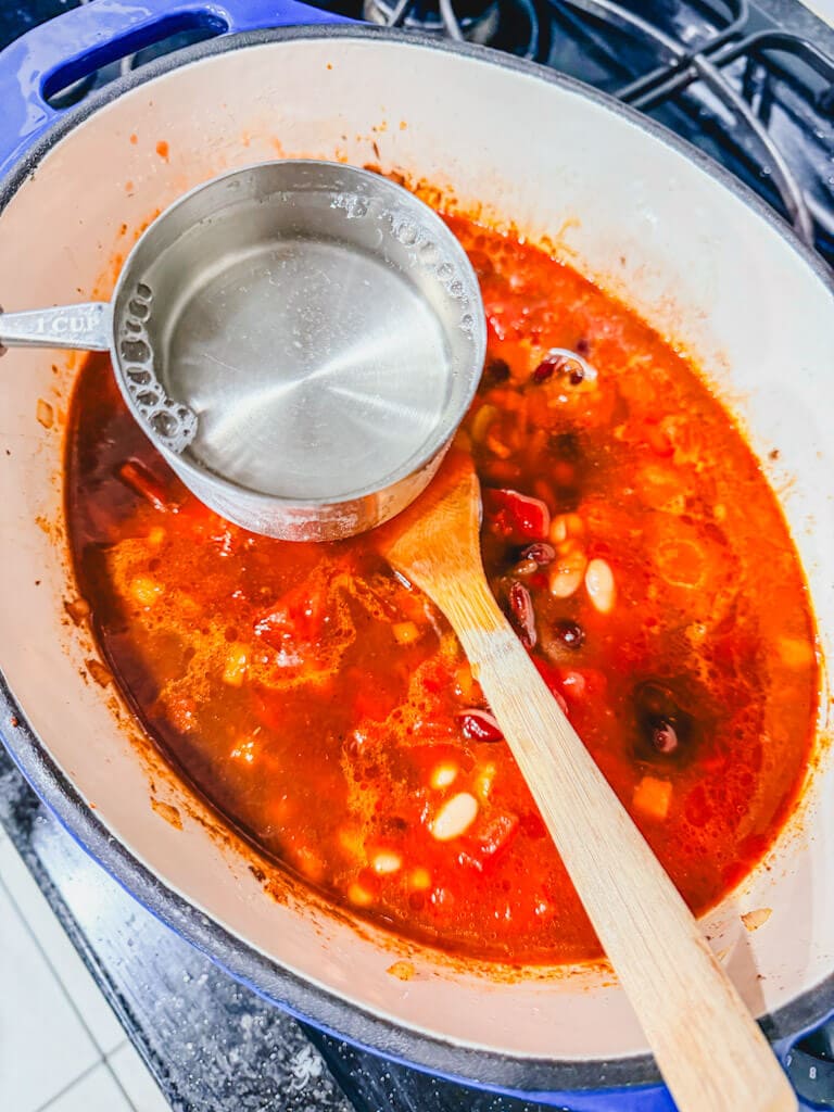 Water in a measuring cup being held over the pot.