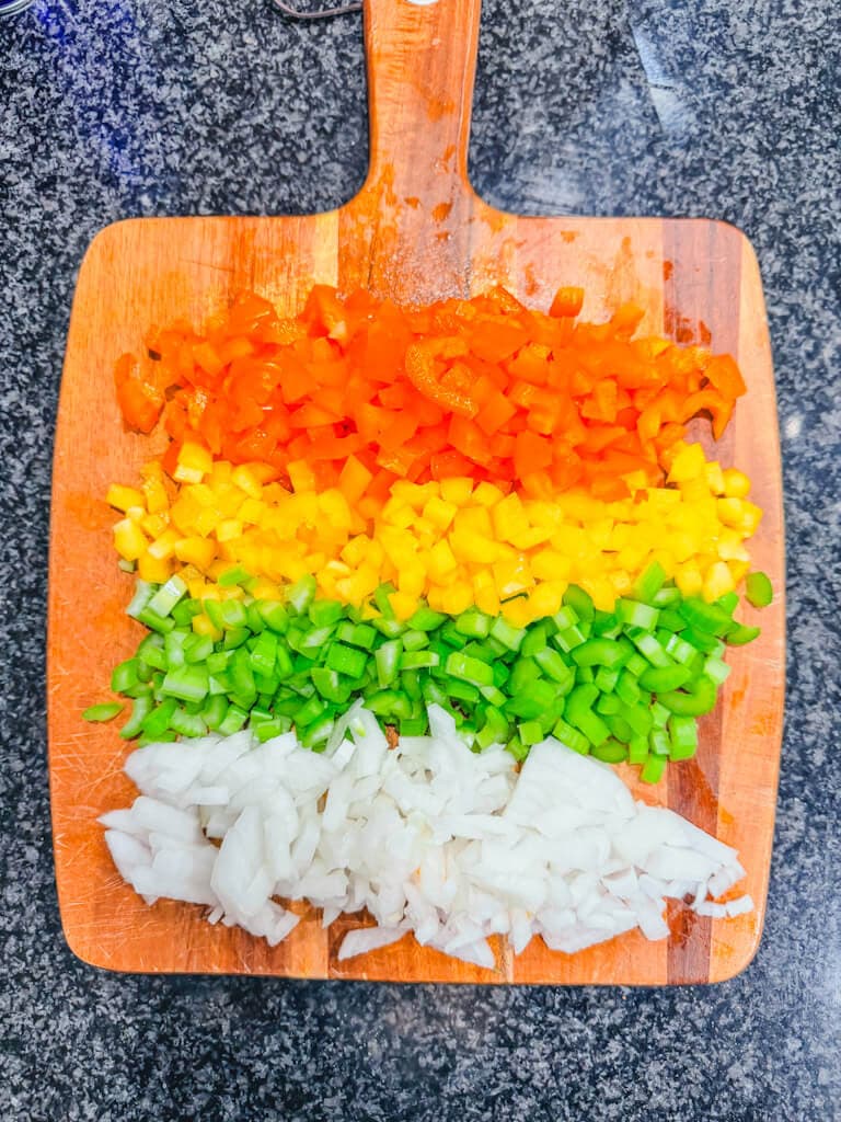 Diced bell peppers, celery, and onions on a cutting board ready to be added to the Dutch oven.
