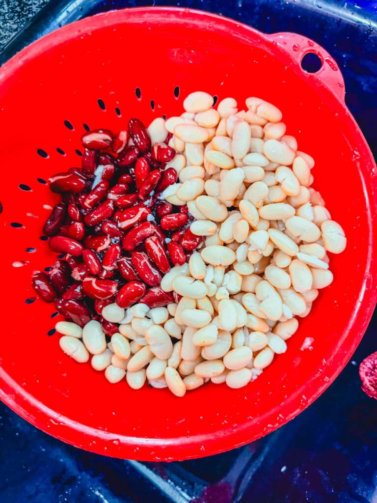 White beans and kidney beans in a red colander draining after being rinsed.