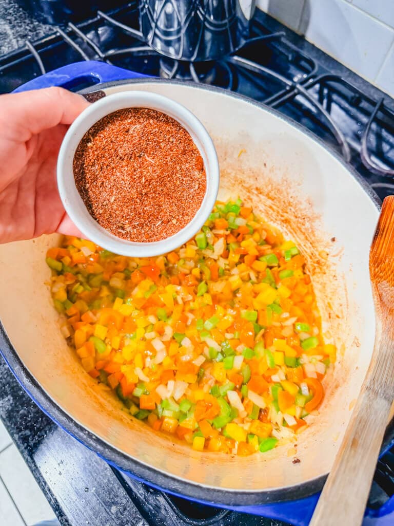 A small bowl of the chili seasoning being held over the vegetables ready to be poured in.