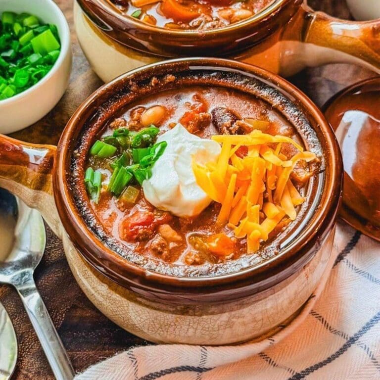 close up of chili beans in a small ceramic soup bowl with sour cream, cheese, and green onions over the top.