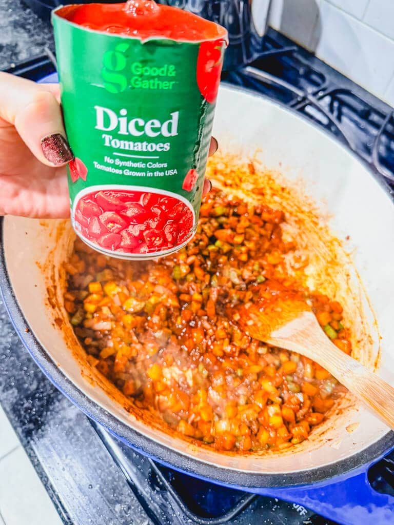 A can of diced tomatoes being held over the Dutch oven.