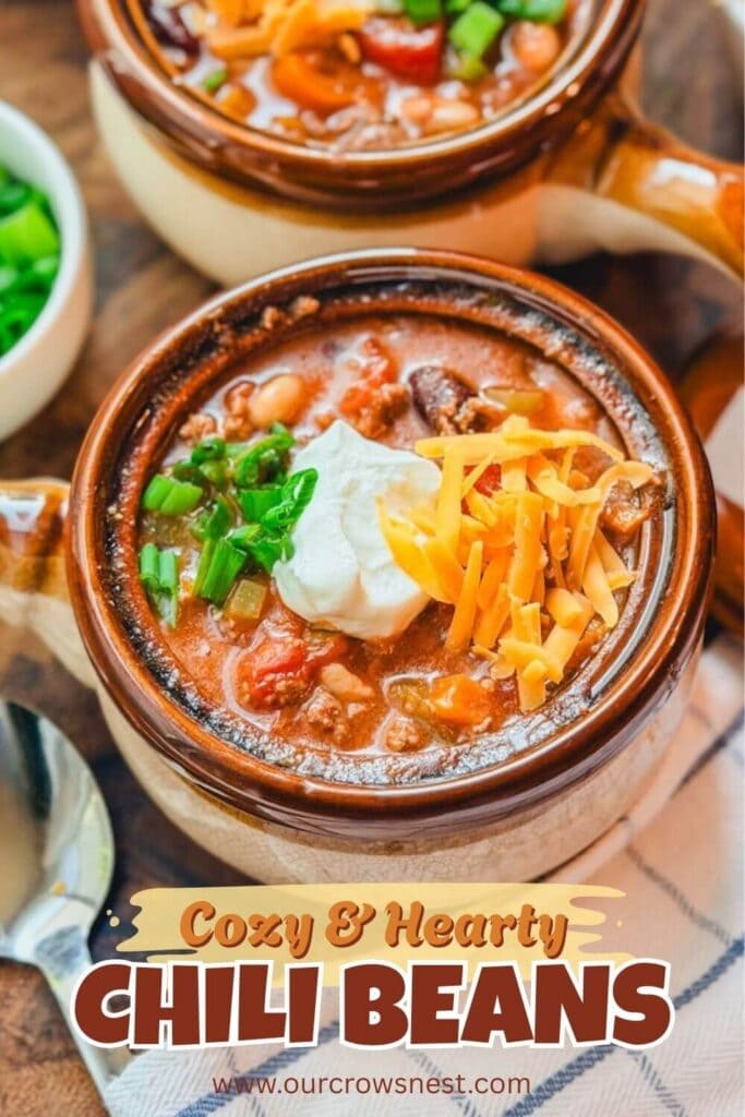 close up of a serving of chili beans in a brown and tan ceramic bowl with cheese, sour cream, and green onions on top of the chili.