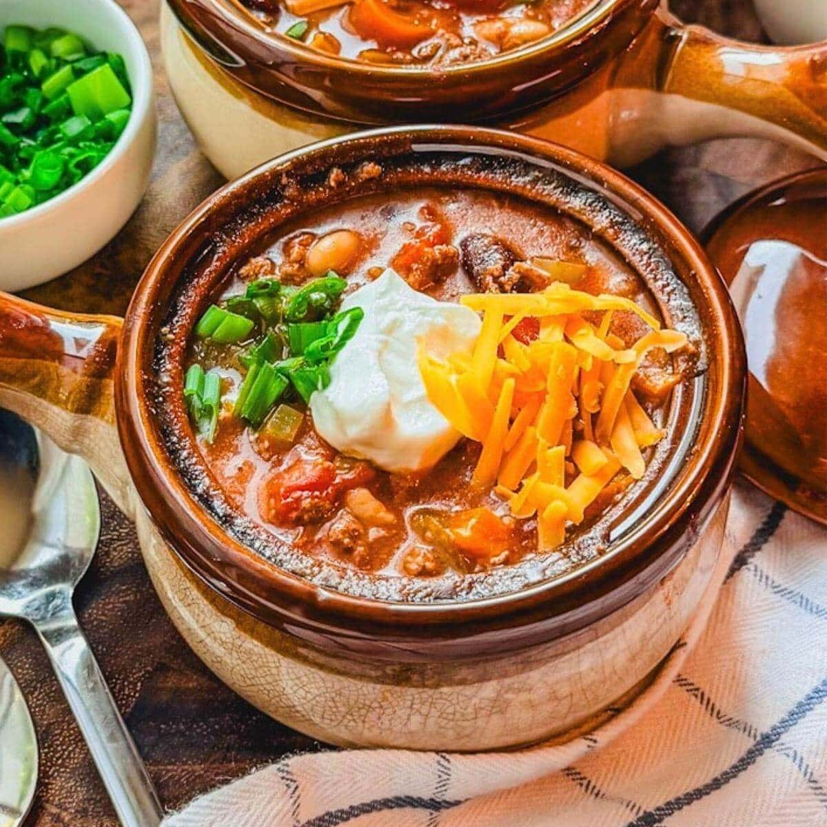 close up of chili beans in a small ceramic soup bowl with sour cream, cheese, and green onions over the top.