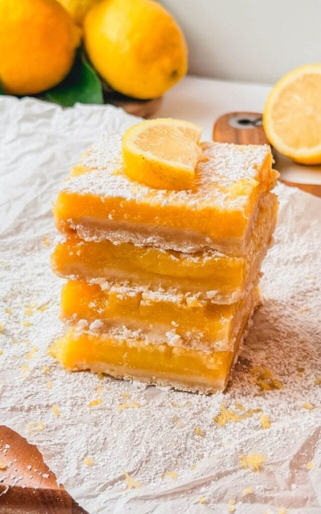 Four lemon bars stacked neatly on top of each other with powdered sugar and lemon zest.