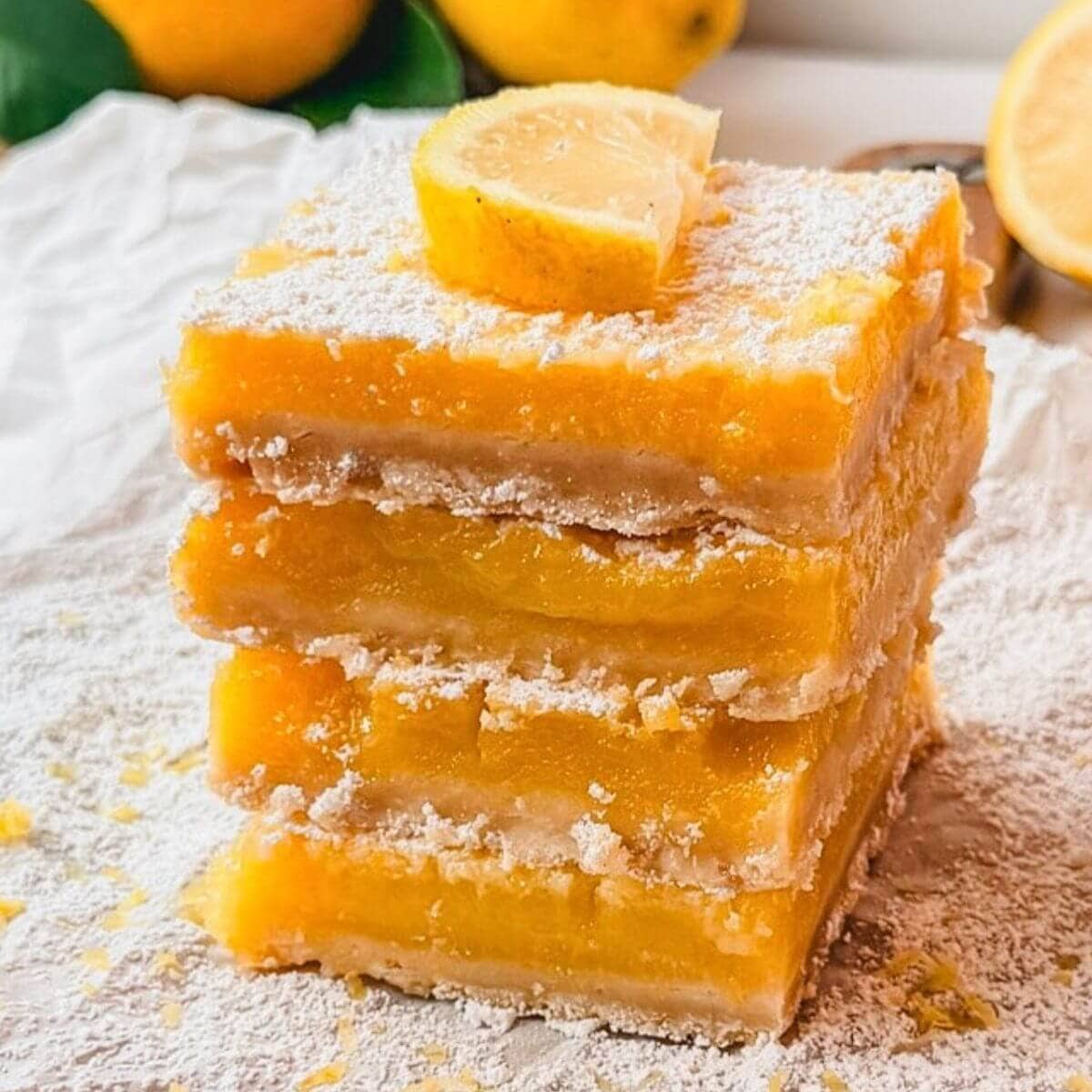 close up of four homemade lemon bars in a stack with a small slice of lemon on top of the top lemon bar.