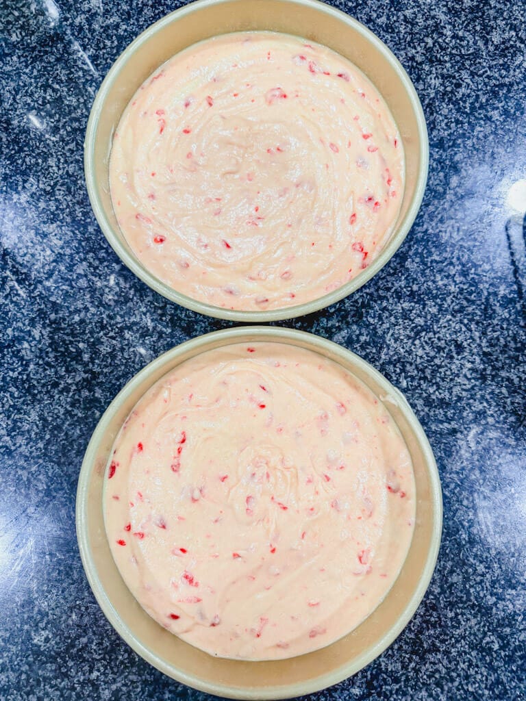 Cake batter that has been added to two greased cake pans ready to be baked.