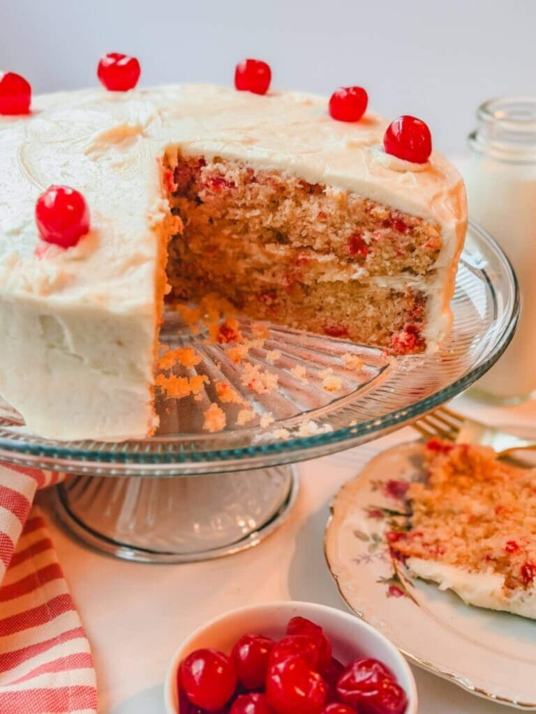 close up view of Betty Crocker Cherry Chip Cake on a cake stand with a large chunk of cake taken out to show what the inside looks like.