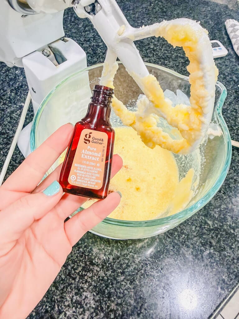 A bottle of almond extract being held over the glass mixing bowl.
