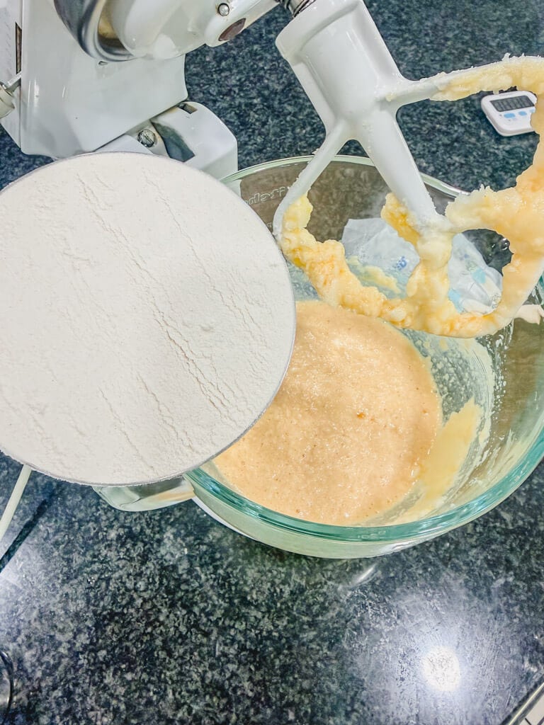 A cup of plain white flour being held over the bowl.