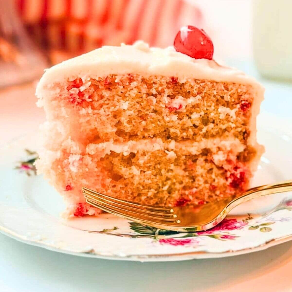 close up of a slice of Betty Crocker Cherry Chip Cake on a floral plate next to a gold spoon.