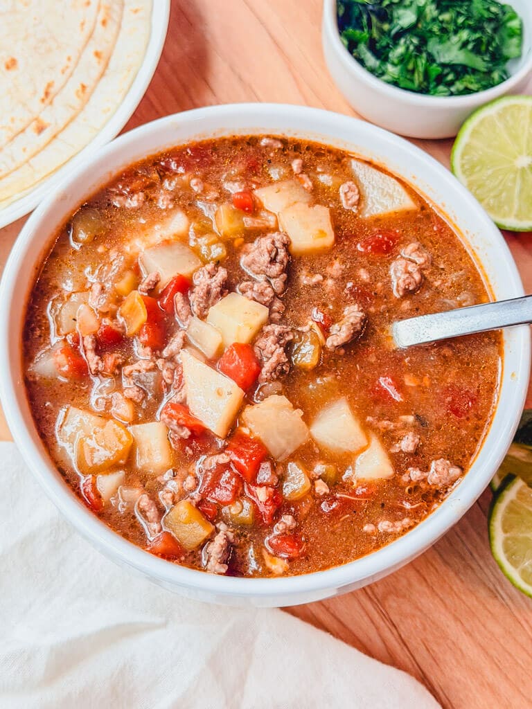 overhead image of ground beef chile stew in a white soup bowl.