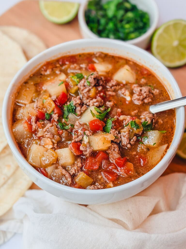 close up of a serving of ground beef chile stew in a white bowl.