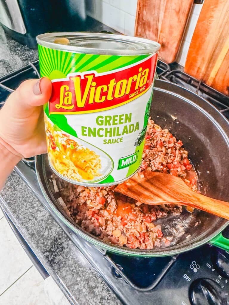 A can of green enchilada sauce being held over the pot.
