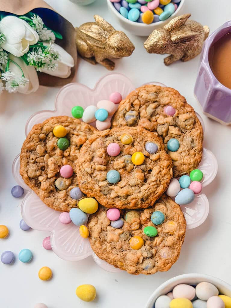 overhead view of 4 monster cookies on a plate next to two golden bunny props and a bouquet of white tulips.