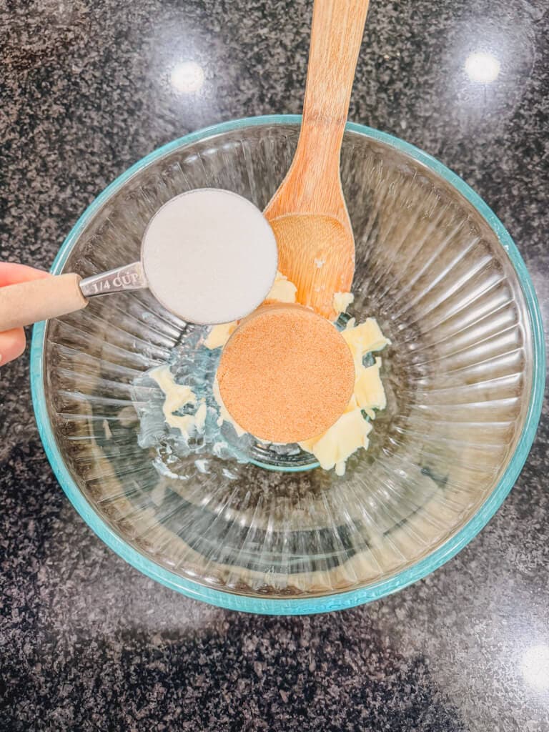 A measuring cup filled with white sugar being held over the bowl.