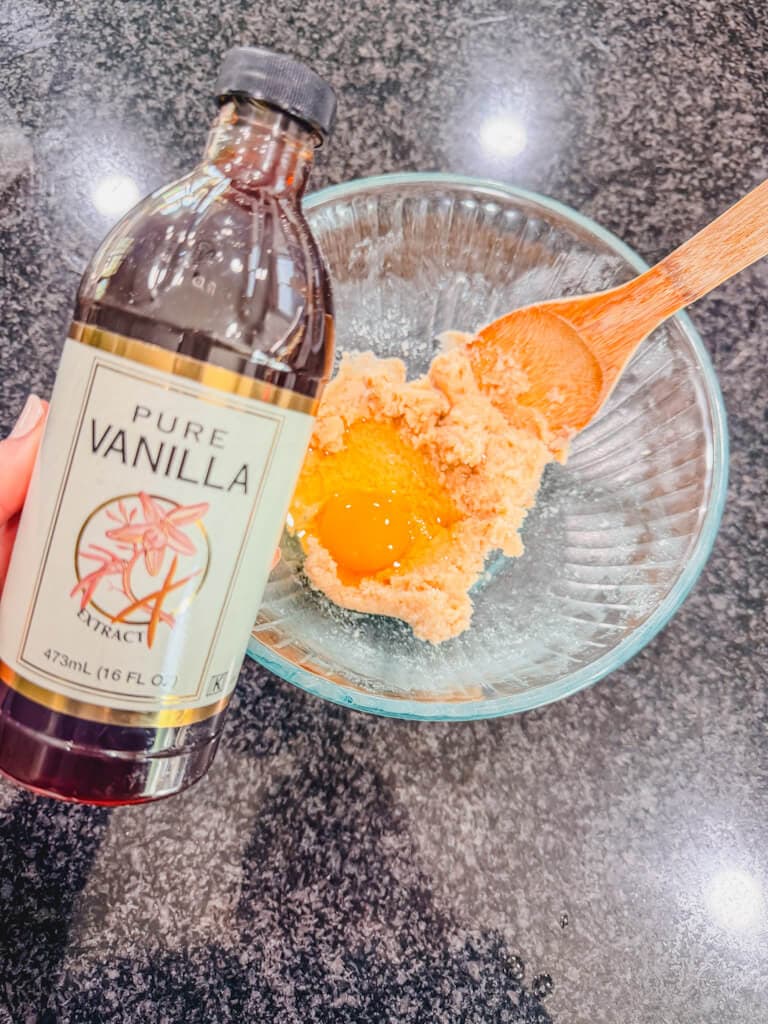 A bottle of vanilla extract being held over the mixing board.