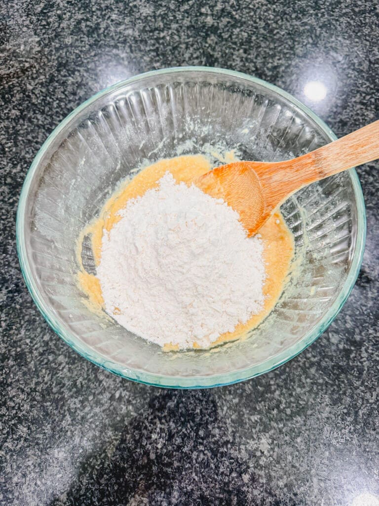 White all-purpose flour added to the wet ingredients in a glass mixing bowl.